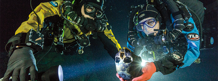 Photograph of two divers. One of the divers is holding a human skull.
