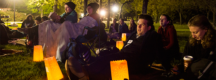 Students sitting on the lawn at night with lanterns.