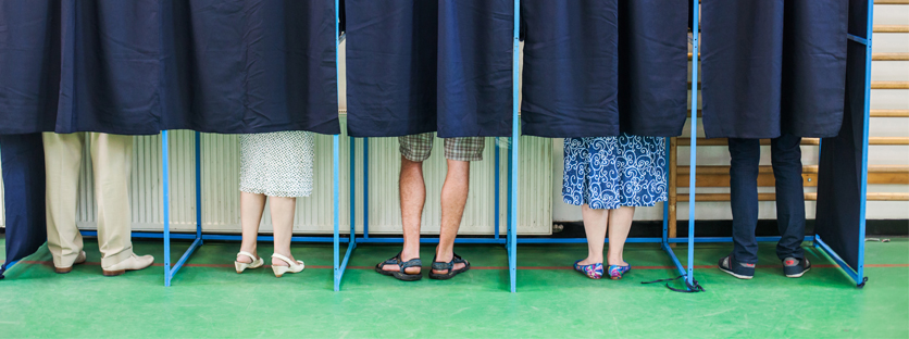 Multiple pairs of legs behind curtains at voting booths