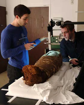 Two scientists examine the mummy and wrappings.